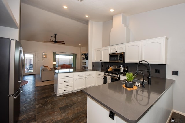 kitchen with a peninsula, stainless steel appliances, white cabinetry, dark countertops, and open floor plan