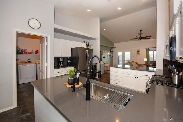 kitchen with a peninsula, a sink, stainless steel appliances, dark countertops, and washing machine and dryer