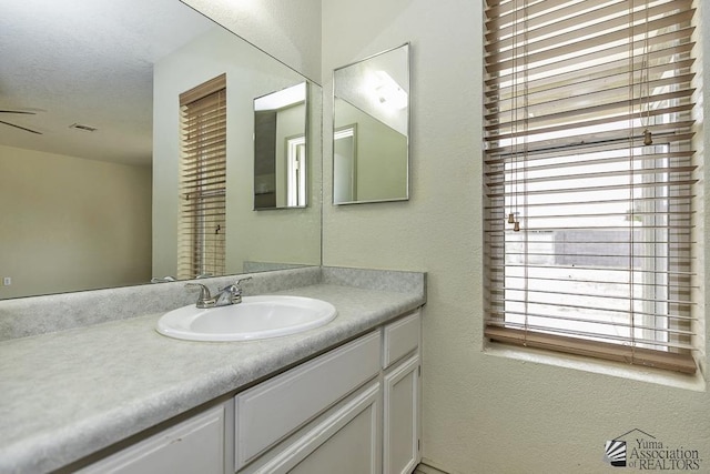 bathroom featuring a textured wall, visible vents, a textured ceiling, and vanity