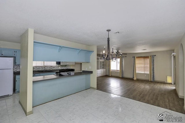 kitchen with open floor plan, freestanding refrigerator, blue cabinets, an inviting chandelier, and a sink