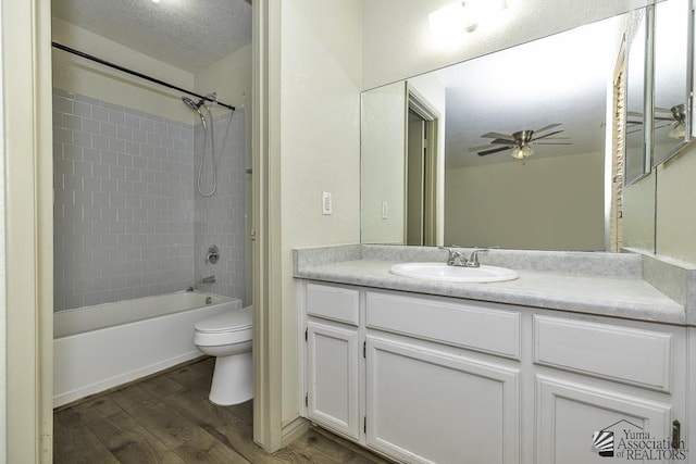 bathroom with a textured ceiling, ceiling fan, toilet, wood finished floors, and vanity