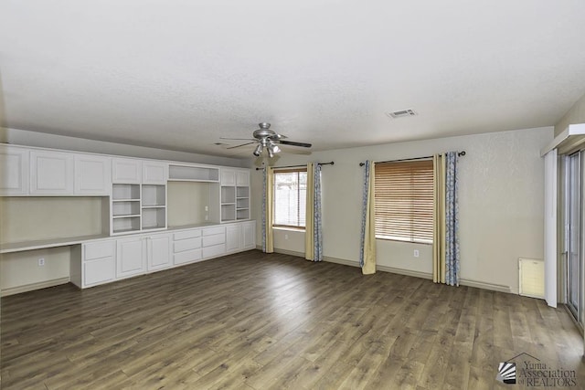 unfurnished living room with ceiling fan, visible vents, built in study area, and dark wood finished floors