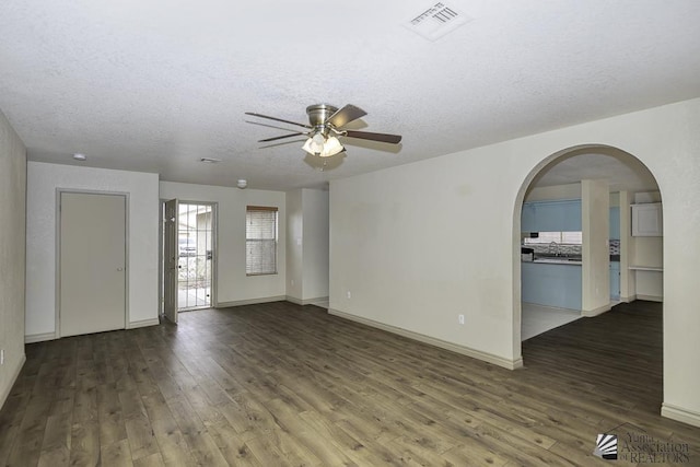 empty room featuring arched walkways, visible vents, a textured ceiling, and wood finished floors