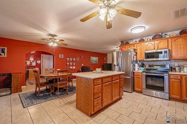 kitchen featuring decorative backsplash, a textured ceiling, stainless steel appliances, light tile patterned floors, and a kitchen island