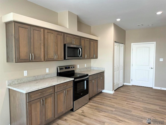 kitchen with dark brown cabinetry, appliances with stainless steel finishes, and light hardwood / wood-style floors