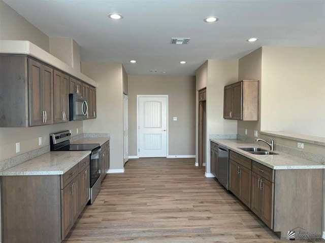 kitchen with stainless steel appliances, light stone countertops, sink, and light hardwood / wood-style flooring