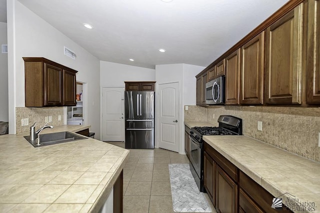 kitchen with appliances with stainless steel finishes, tasteful backsplash, sink, tile countertops, and light tile patterned flooring