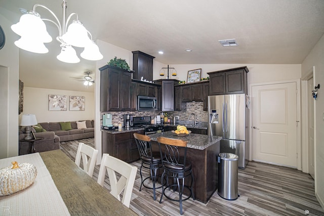 kitchen featuring tasteful backsplash, dark brown cabinetry, stainless steel appliances, wood-type flooring, and a kitchen island