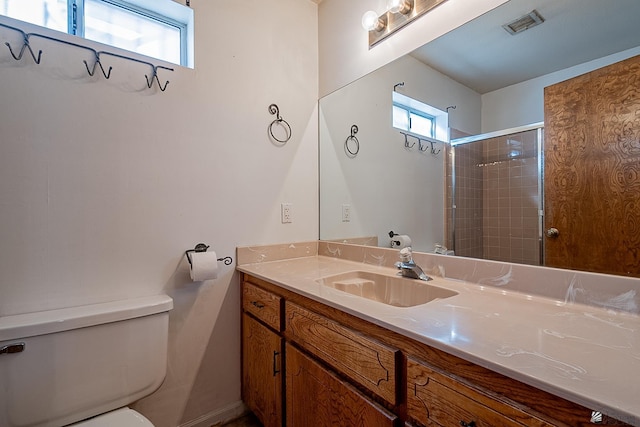 bathroom with a healthy amount of sunlight, vanity, toilet, and tiled shower