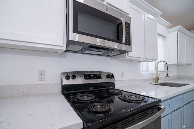 kitchen with appliances with stainless steel finishes, light stone counters, blue cabinets, sink, and white cabinets