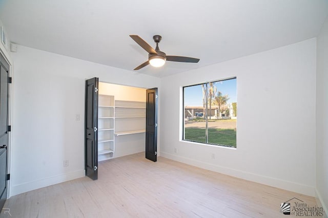 unfurnished bedroom featuring a walk in closet, a closet, light hardwood / wood-style flooring, and ceiling fan