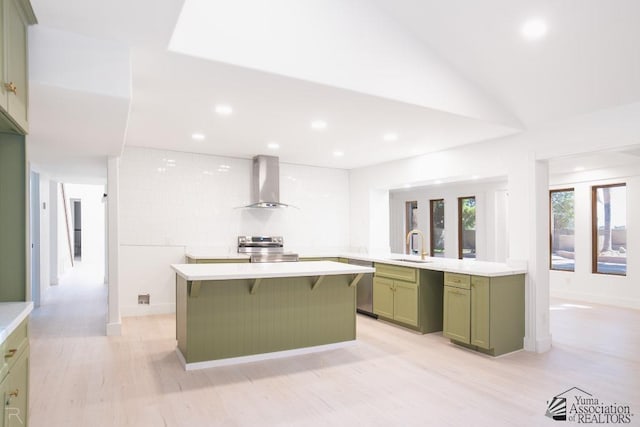 kitchen with a center island, light countertops, green cabinets, a sink, and wall chimney range hood