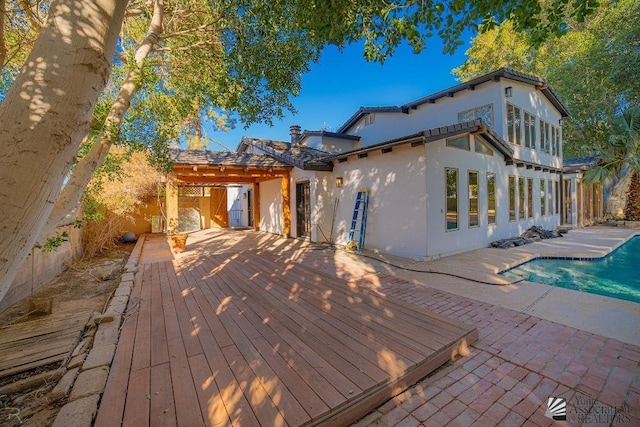 rear view of property with a patio, fence, a wooden deck, and stucco siding