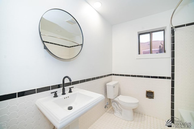 bathroom featuring tile patterned floors, toilet, sink, and tile walls