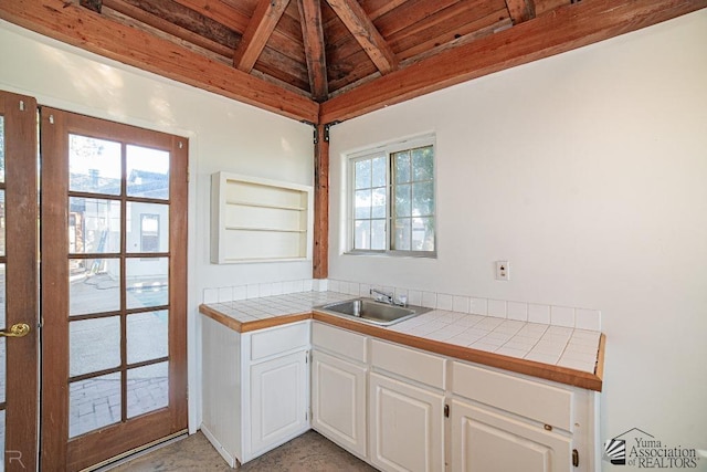 kitchen featuring tile countertops, white cabinetry, a sink, wooden ceiling, and beamed ceiling