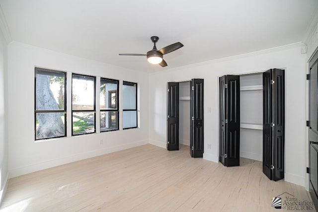 unfurnished bedroom featuring ceiling fan, baseboards, light wood-style floors, two closets, and crown molding