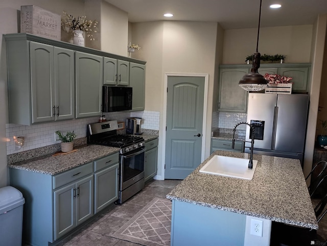 kitchen with backsplash, stainless steel appliances, a kitchen island with sink, sink, and decorative light fixtures