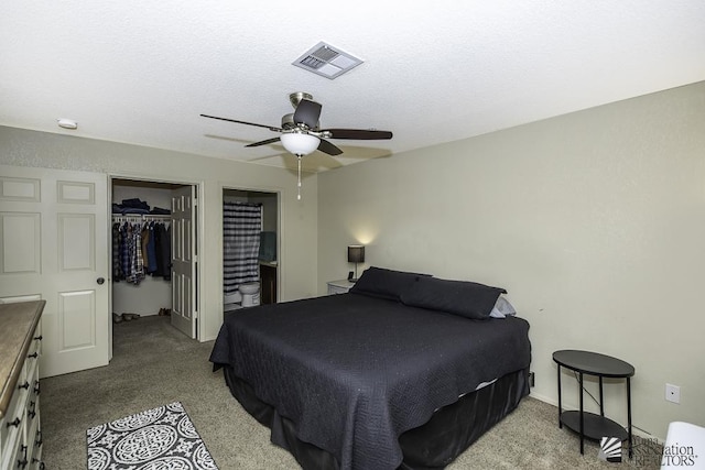 carpeted bedroom featuring visible vents, a walk in closet, a closet, ensuite bath, and a ceiling fan