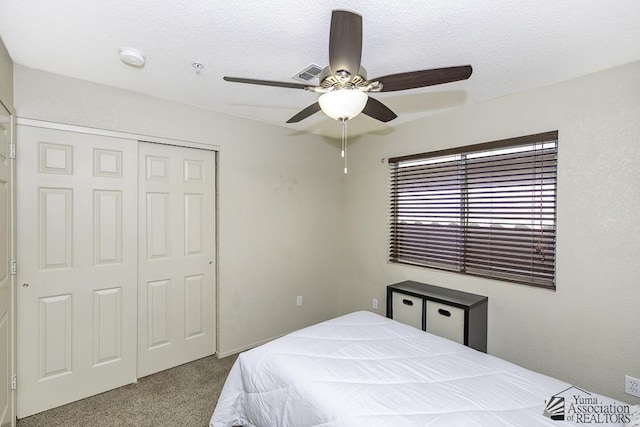 carpeted bedroom featuring a closet, a textured ceiling, visible vents, and ceiling fan