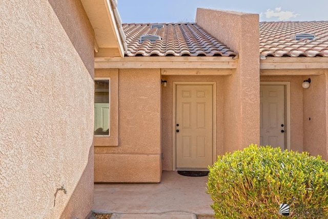 view of exterior entry featuring stucco siding and a tile roof