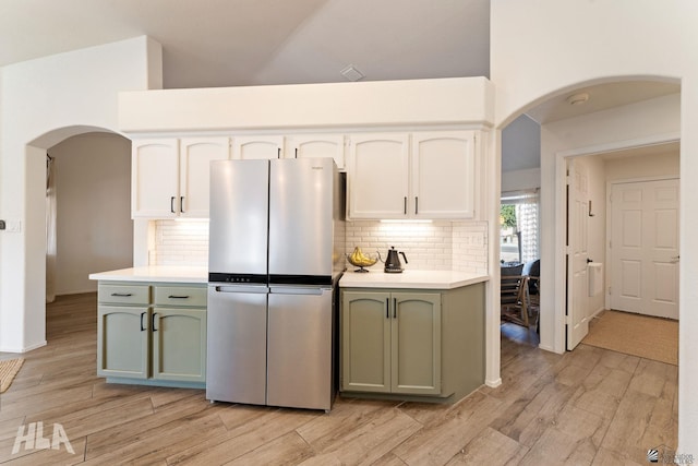 kitchen with light hardwood / wood-style flooring, stainless steel refrigerator, green cabinets, white cabinetry, and backsplash