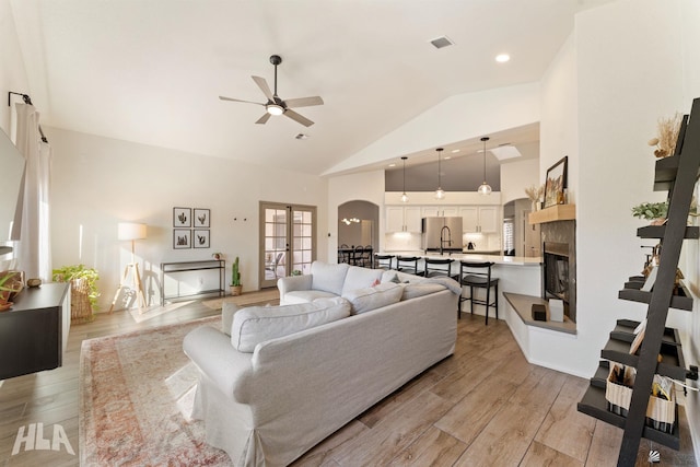 living room featuring light hardwood / wood-style flooring, high vaulted ceiling, french doors, and ceiling fan