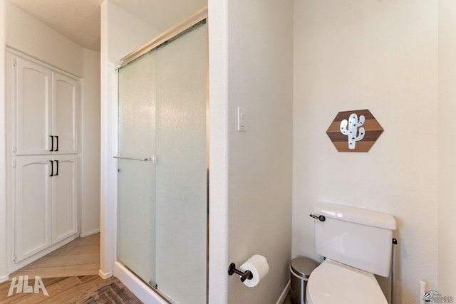 bathroom featuring hardwood / wood-style floors, a shower with door, and toilet