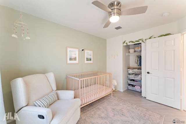 bedroom featuring a nursery area, ceiling fan with notable chandelier, light hardwood / wood-style floors, and a closet