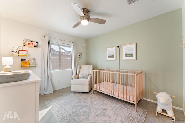 bedroom featuring a crib, light hardwood / wood-style floors, and ceiling fan