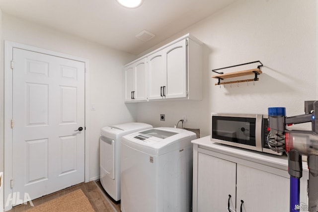 washroom with cabinets, wood-type flooring, and separate washer and dryer