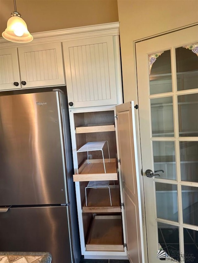 interior space featuring stainless steel refrigerator, decorative light fixtures, and white cabinetry