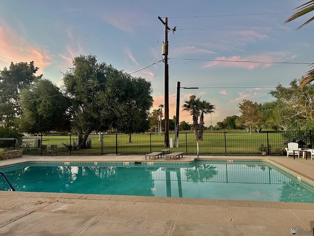 pool at dusk with a patio area and a lawn