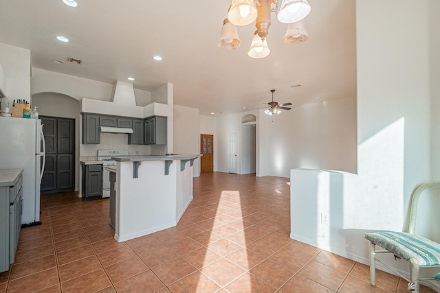 kitchen with gray cabinetry, white appliances, a breakfast bar, light tile patterned flooring, and ceiling fan with notable chandelier