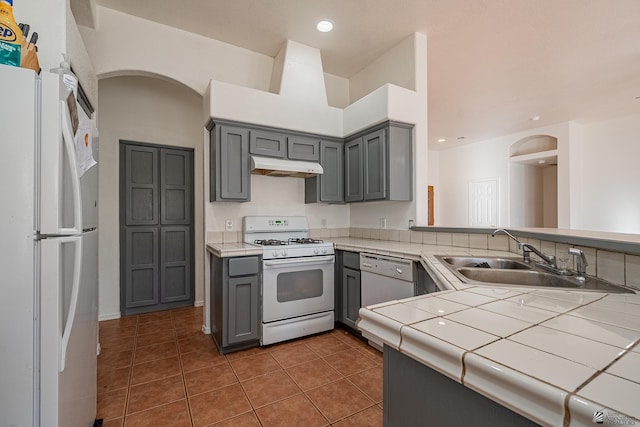 kitchen with tile counters, sink, kitchen peninsula, white appliances, and gray cabinets