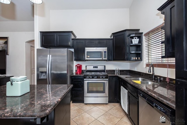 kitchen with arched walkways, light tile patterned flooring, a sink, appliances with stainless steel finishes, and dark stone countertops