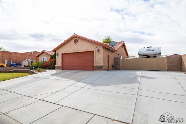 mediterranean / spanish-style home with an attached garage, a tile roof, concrete driveway, a gate, and stucco siding