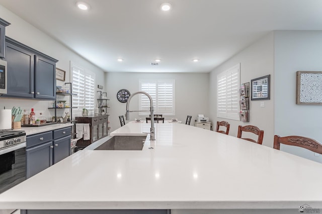 kitchen with sink, gray cabinetry, a breakfast bar area, a large island with sink, and stainless steel appliances