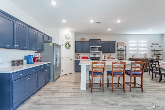 kitchen with blue cabinets, an island with sink, appliances with stainless steel finishes, and a breakfast bar area