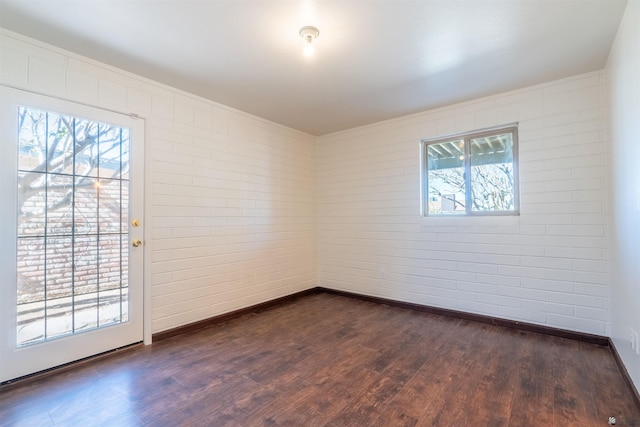 unfurnished room with dark wood-type flooring, a healthy amount of sunlight, and brick wall