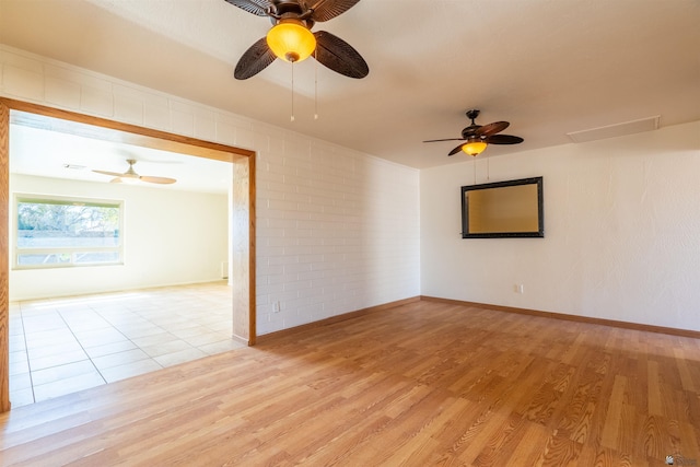 spare room with ceiling fan, brick wall, and light wood-type flooring