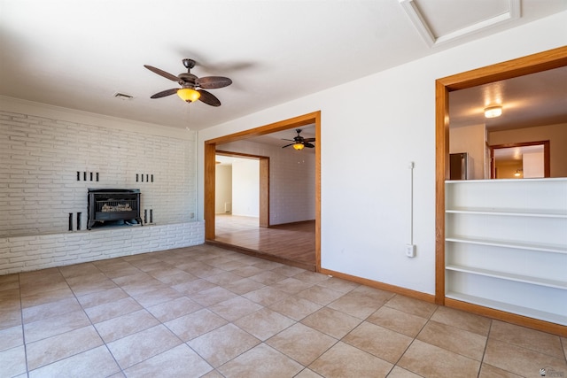 unfurnished living room featuring ceiling fan, brick wall, light tile patterned floors, and a wood stove