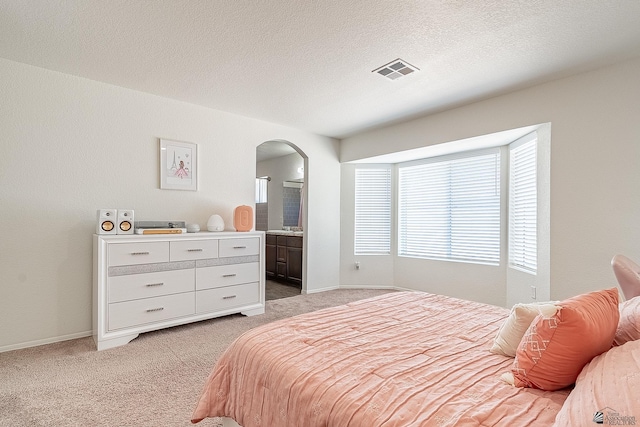 carpeted bedroom with connected bathroom and a textured ceiling