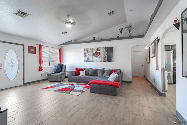 living room featuring light wood-type flooring, arched walkways, visible vents, and vaulted ceiling