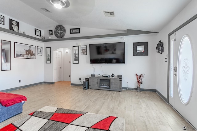 living area with visible vents, arched walkways, baseboards, lofted ceiling, and light wood-style floors