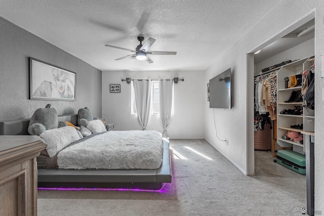 carpeted bedroom featuring a textured wall, a spacious closet, a ceiling fan, a textured ceiling, and baseboards