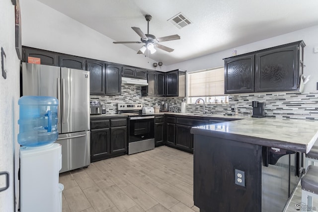 kitchen with lofted ceiling, under cabinet range hood, visible vents, appliances with stainless steel finishes, and backsplash