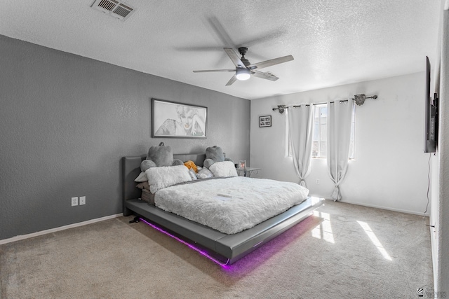 carpeted bedroom featuring visible vents, a textured wall, ceiling fan, a textured ceiling, and baseboards