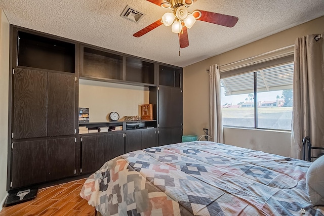 bedroom featuring ceiling fan, visible vents, light wood finished floors, and a textured ceiling