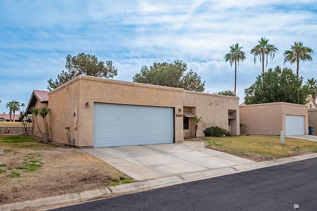 pueblo-style home with stucco siding, driveway, a front yard, and an attached garage