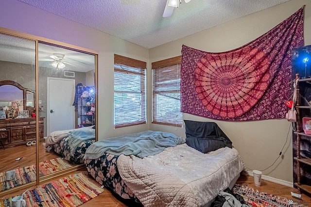 bedroom with wood finished floors, baseboards, a ceiling fan, visible vents, and a textured ceiling